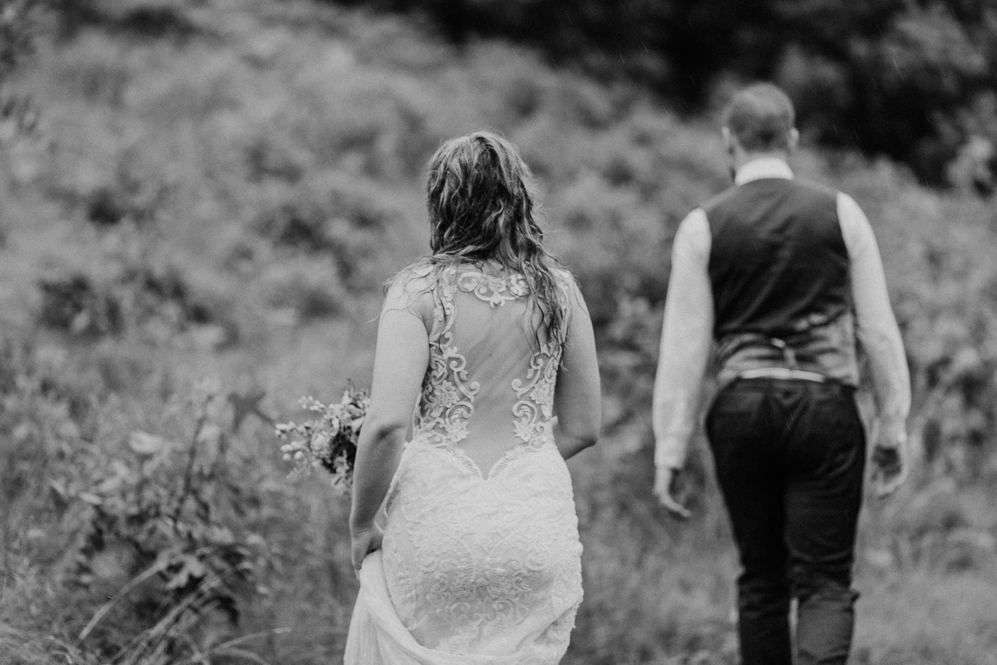 Bride and groom walk through a rainy forest