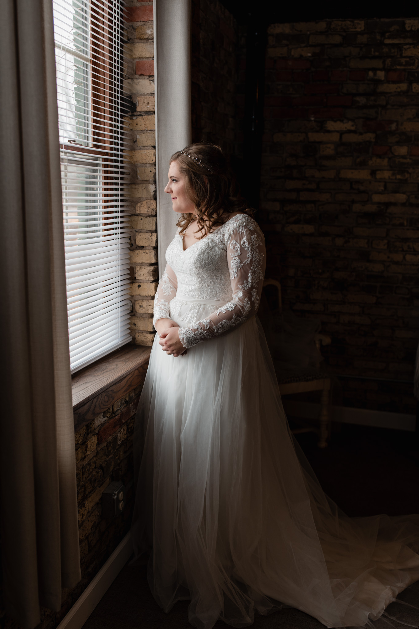 Bride standing in beautiful window light wearing a long sleeve lace gown with tulle skirt at Milwaukee's Ivy House
