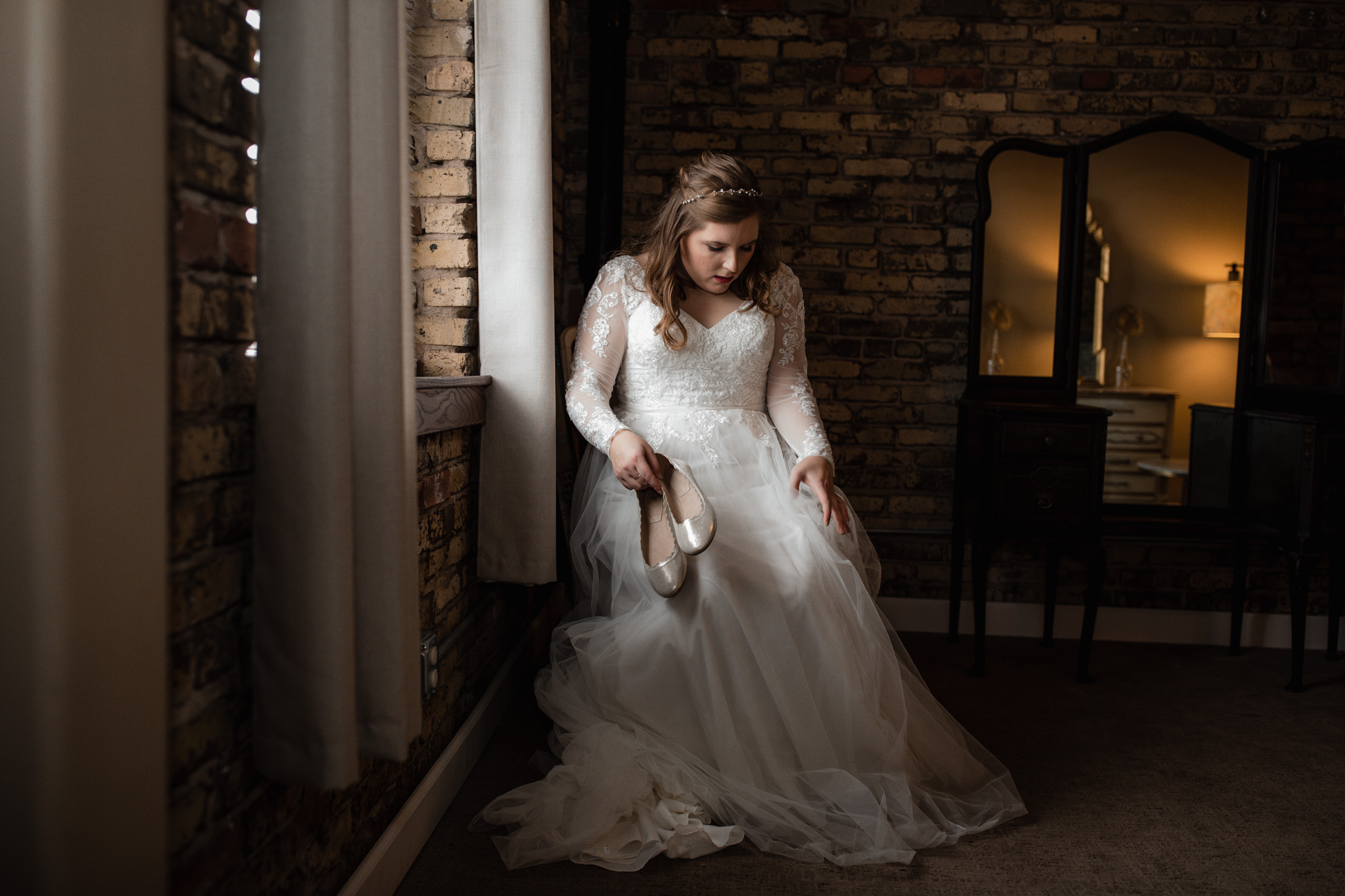 Bride in chiffon tulle wedding gown putting on shoes in the Ivy House getting ready room -milwaukee wedding photographer - good lighting - natural colors editing