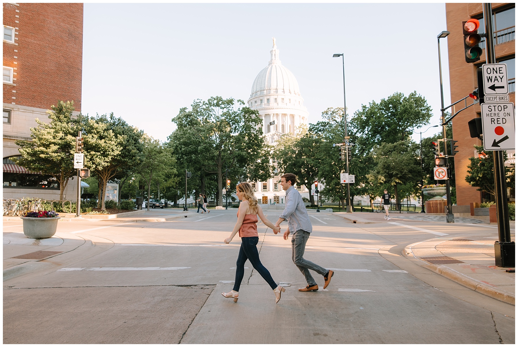 Engaged couple walking across a Madison Wisconsin crosswalk with the state Capitol in the background