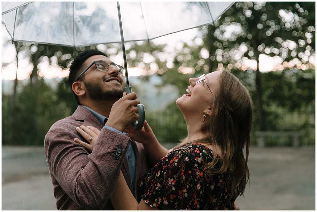 Couple looking up at the cloudy sky as it starts to rain during their engagement pictures