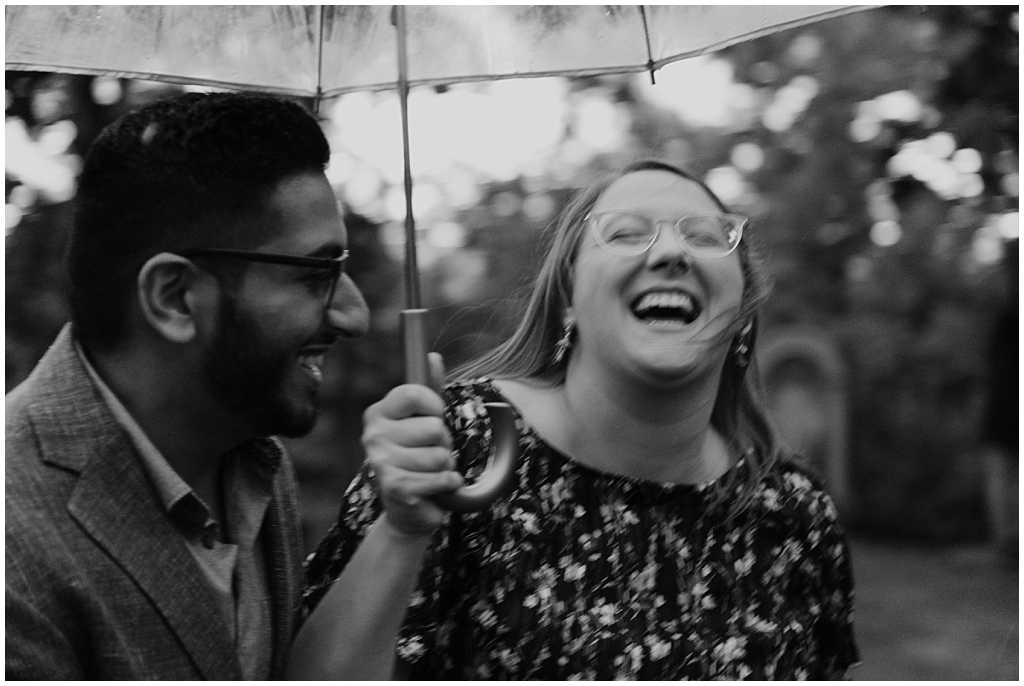 Couple under umbrella getting rained on during engagement session