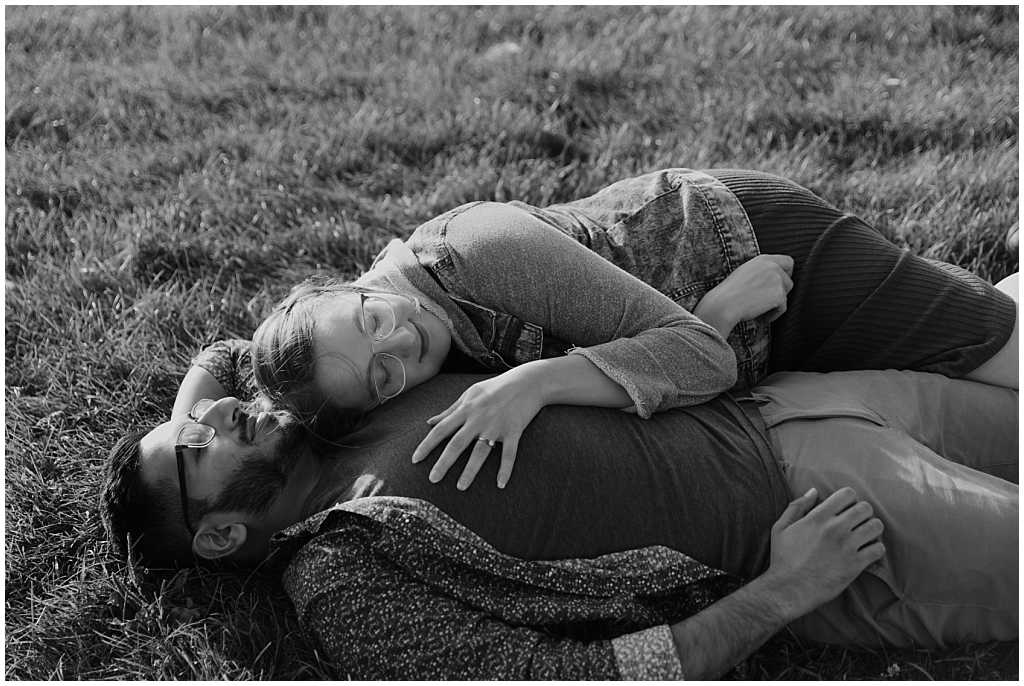Black and white photo of an engaged woman laying on man's chest in the grass