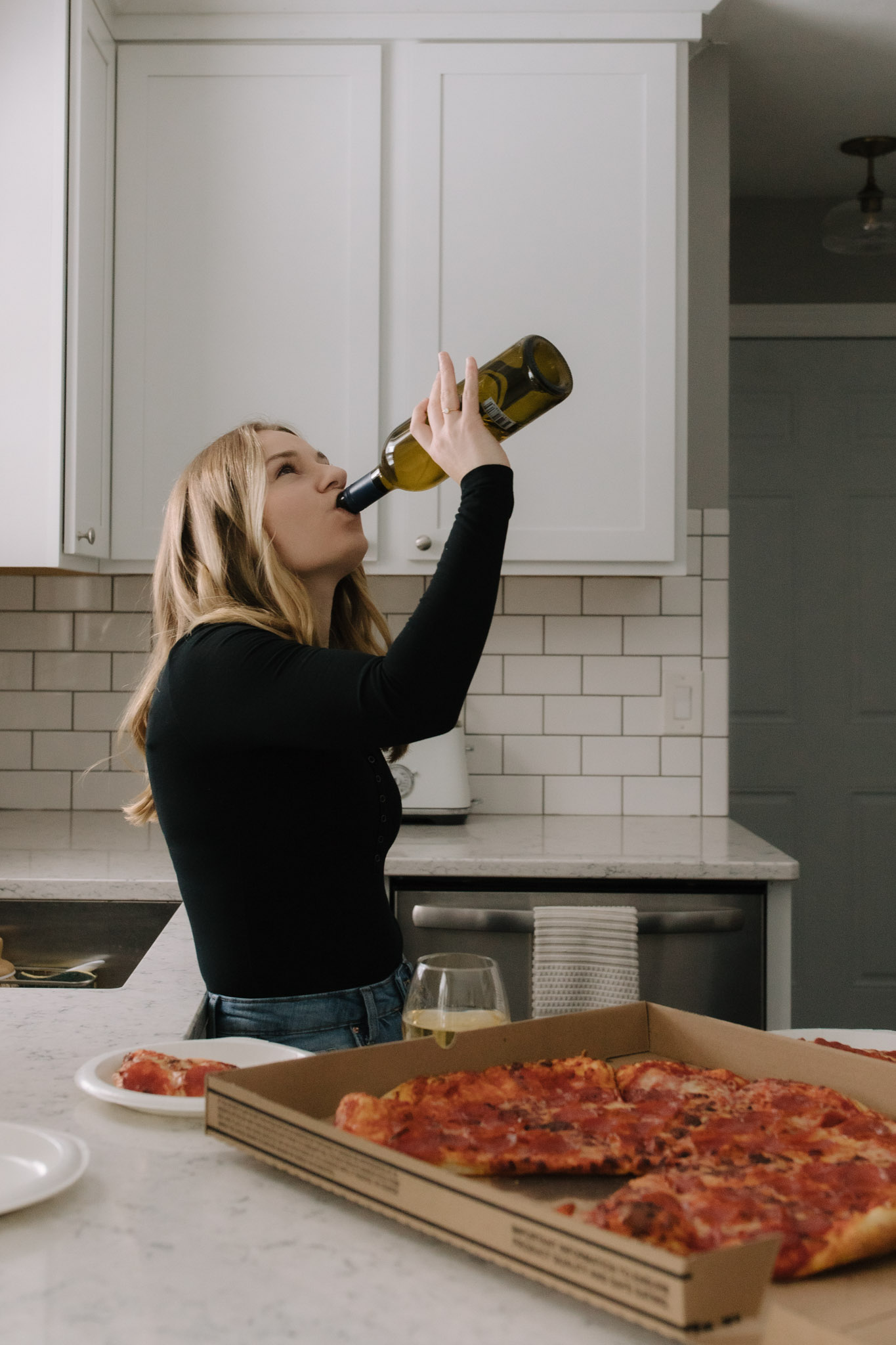 Woman drinking wine and eating pizza in the kitchen of her new Port Washington home