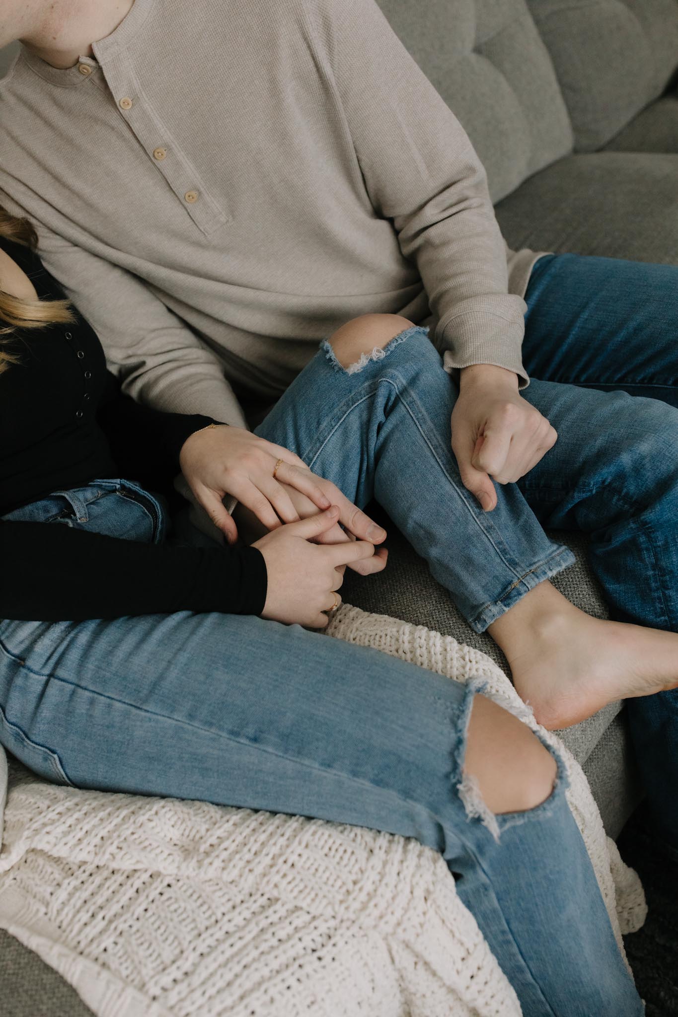Close up of couples hands and legs as they sit on the couch