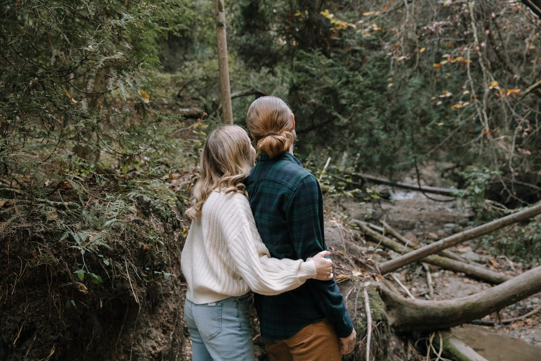 Couple standing in the woods, looking at fallen trees