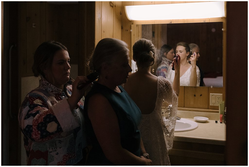 Bride getting ready in cabin while sister helps mom do hair - unique camp wedding inspiration