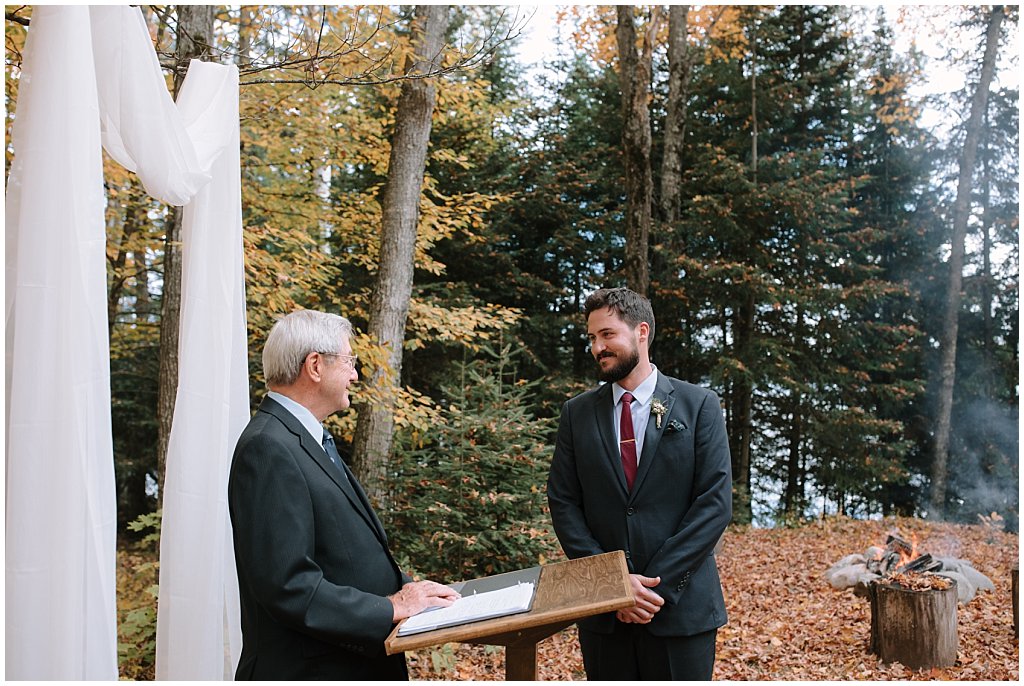Groom at outdoor ceremony in the fall - organza in trees for backdrop - campfire to the side 