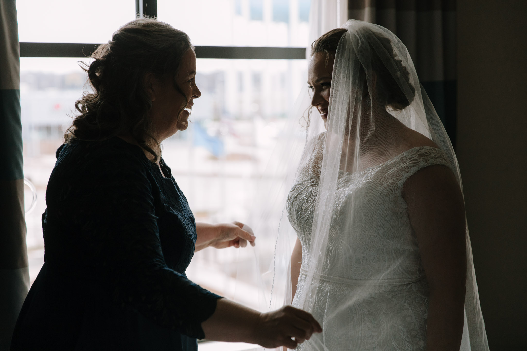 Silhouette of mother placing homemade veil on bride before St Stanislaus church wedding - Hilton Homewood Suites - Wauwatosa