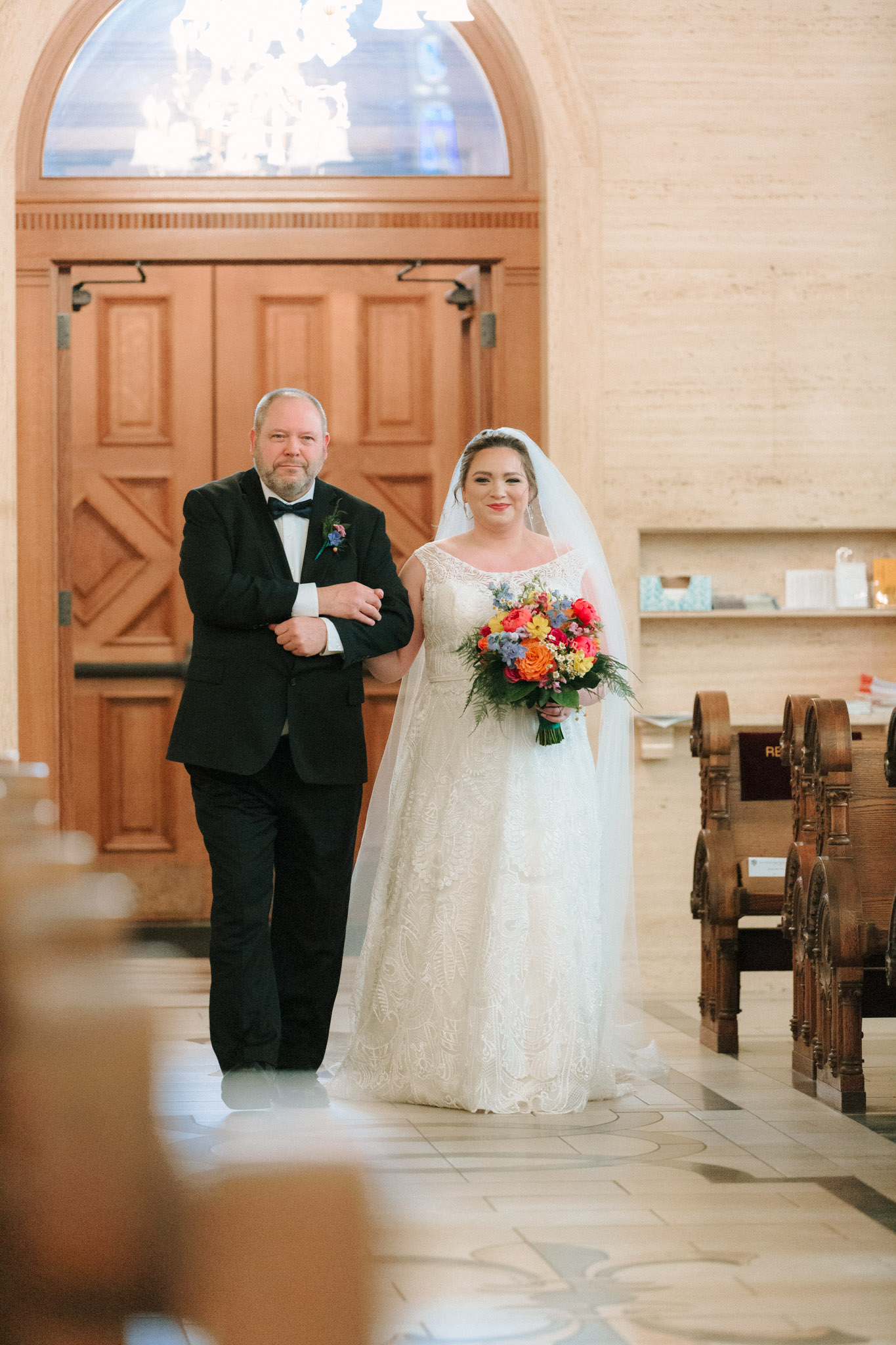 Bride wearing handmade veil with brightly colored flowers walking down aisle with father - St Stanislaus wedding