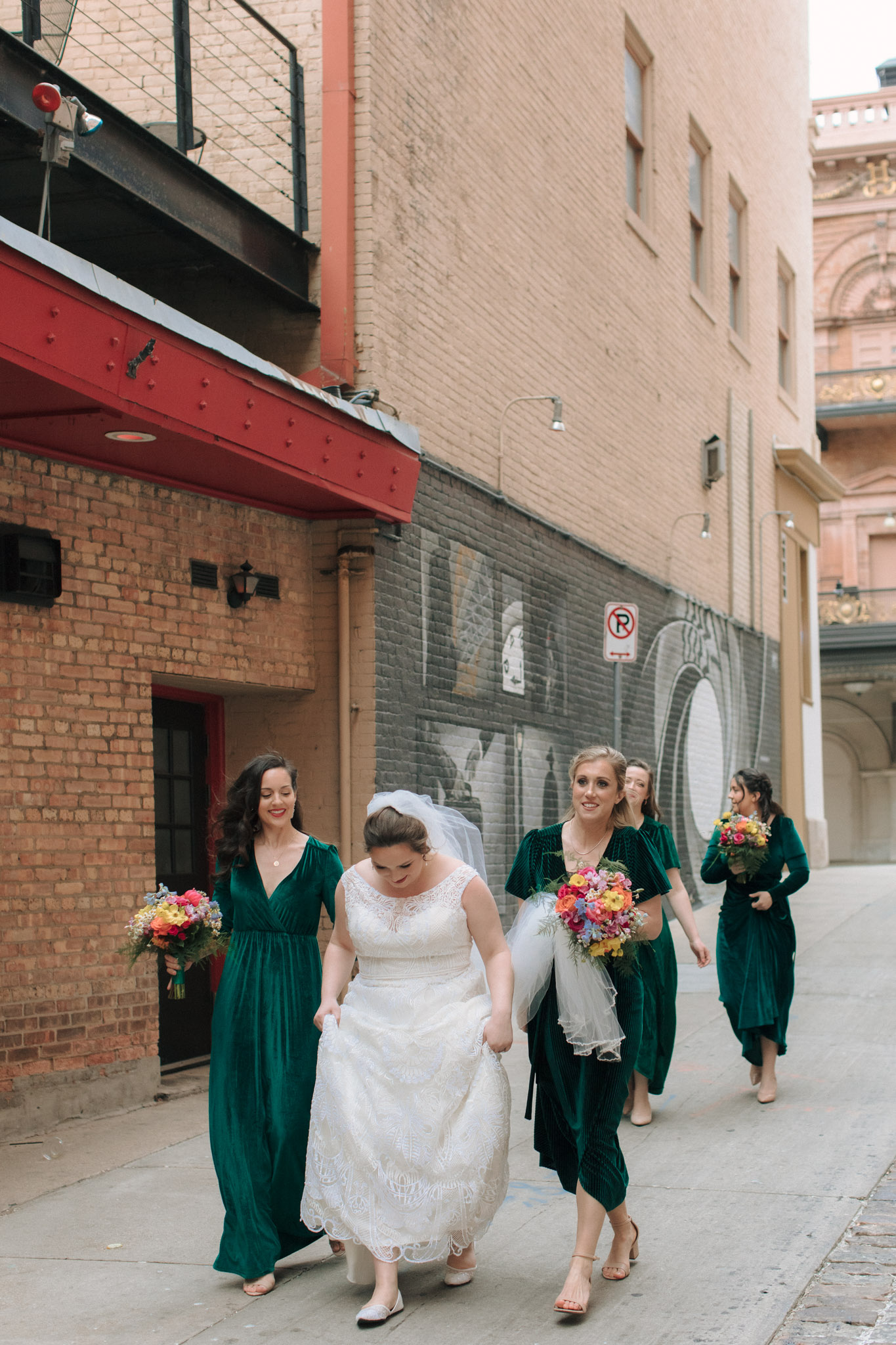 Bridesmaids in emerald dresses with bright flowers outside of Pabst Theatre for wedding pictures