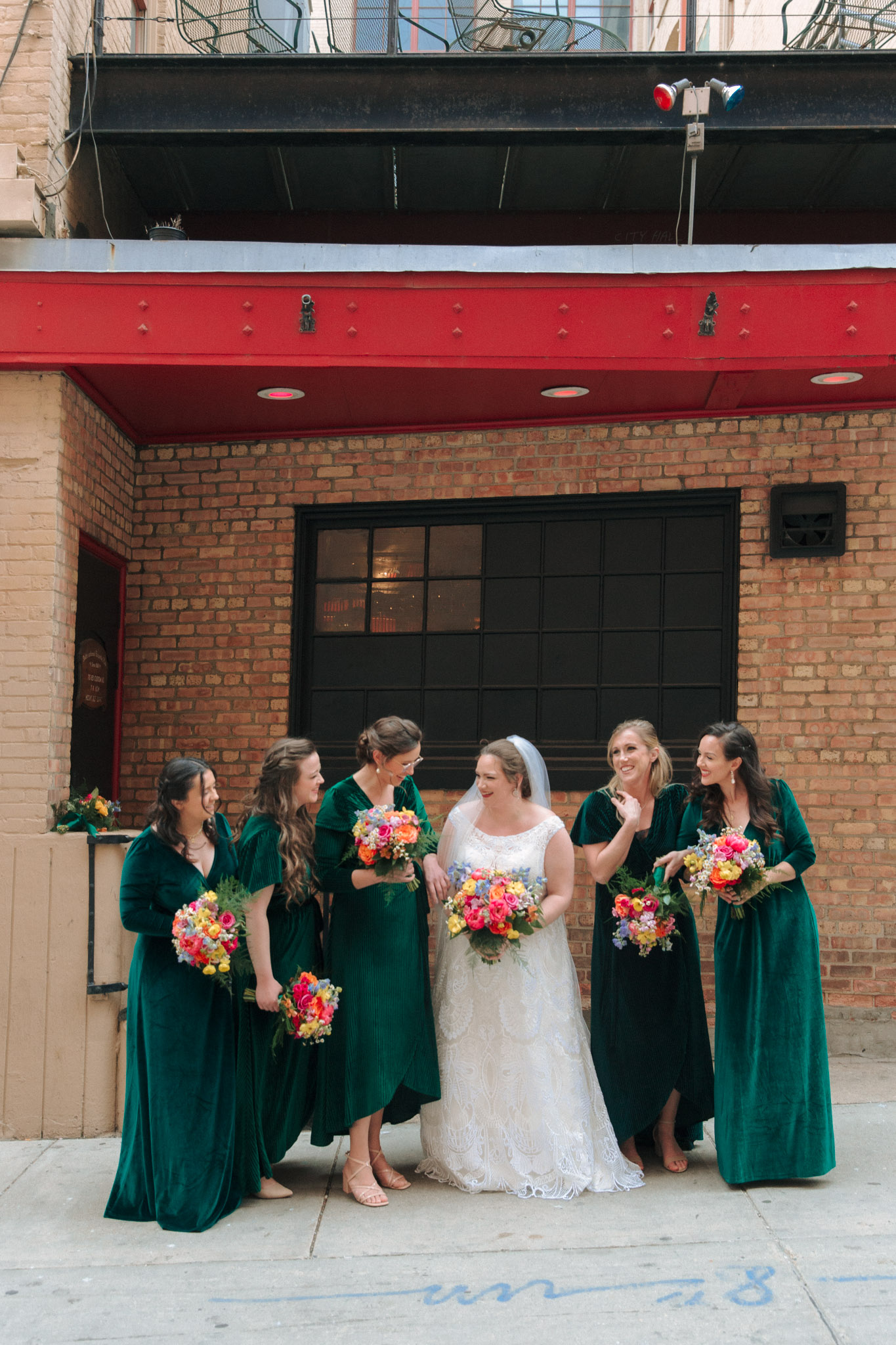 Bridesmaids in emerald dresses with bright flowers outside of Pabst Theatre for wedding pictures