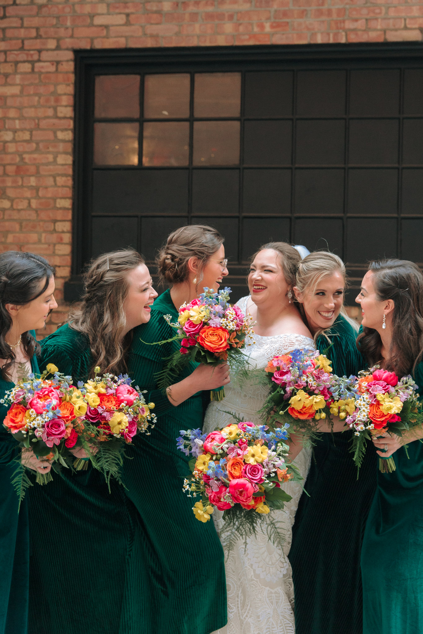 Bridesmaids in emerald dresses with bright flowers outside of Pabst Theatre for wedding pictures