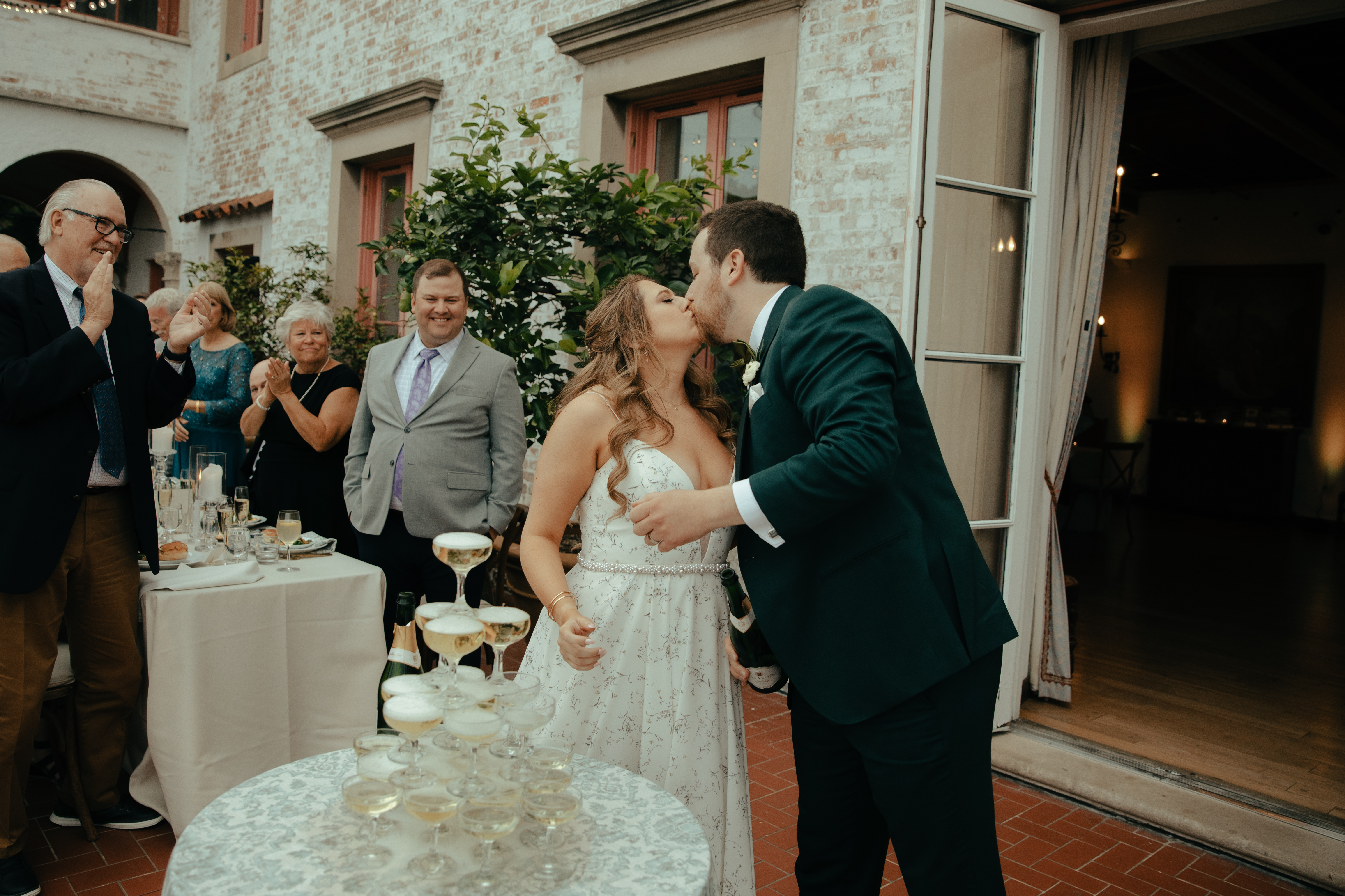Couple kissing in front of a champagne tower at their Villa Terrace Milwaukee weddiing. Bride is wearing a Tara La Tour gown and groom is in emerald suit.