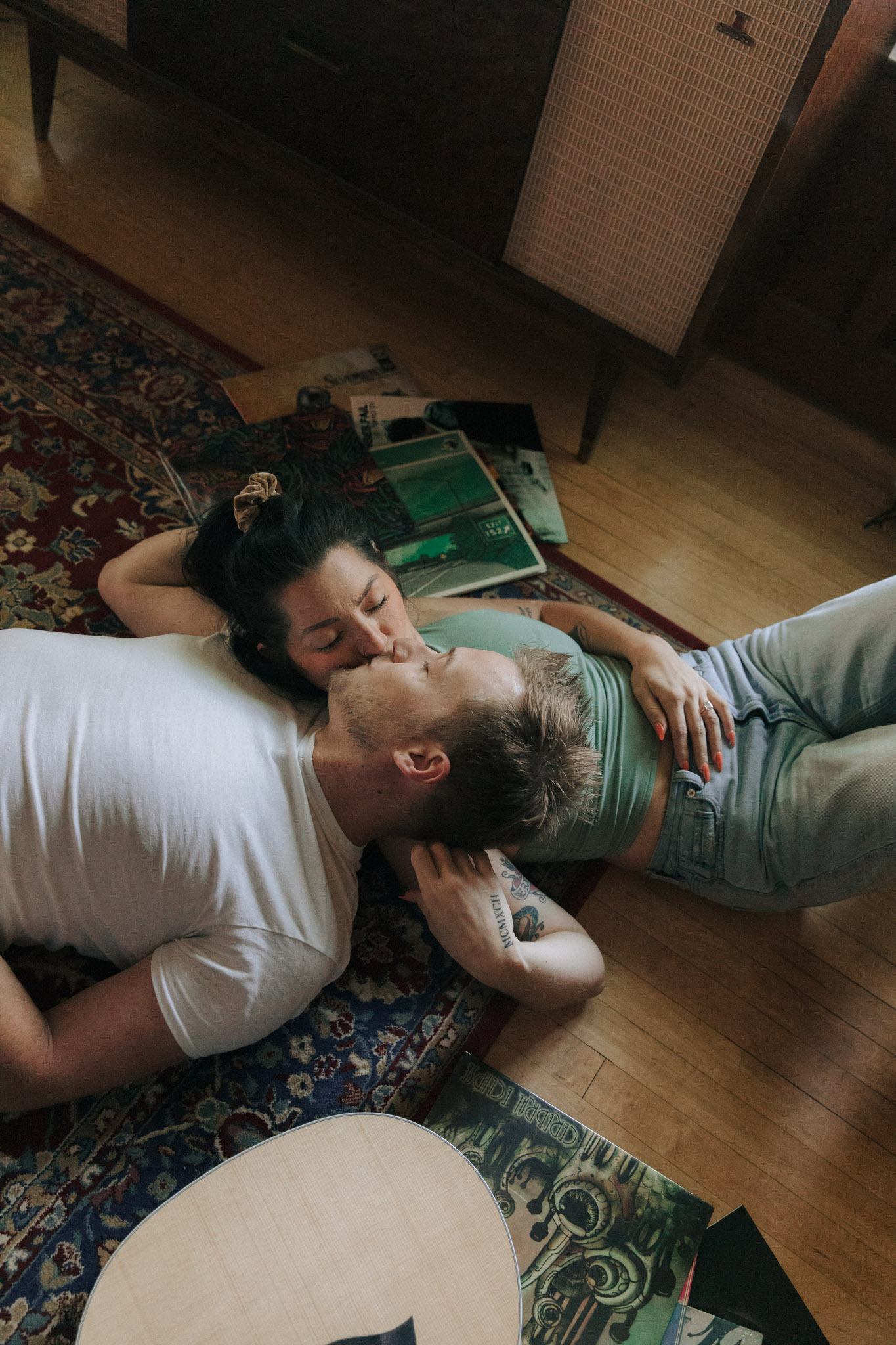 A couple laying on a vintage rug with a guitar and records on the floor