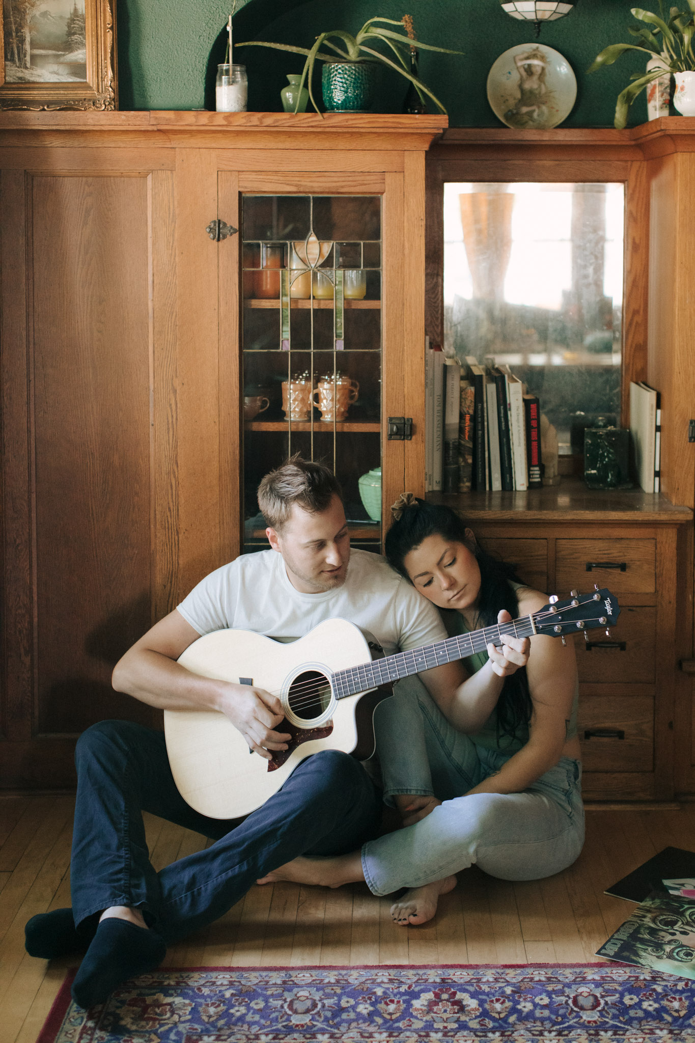 Romantic engagement photo of a couple cuddling while playing guitar on the floor in their Milwaukee home