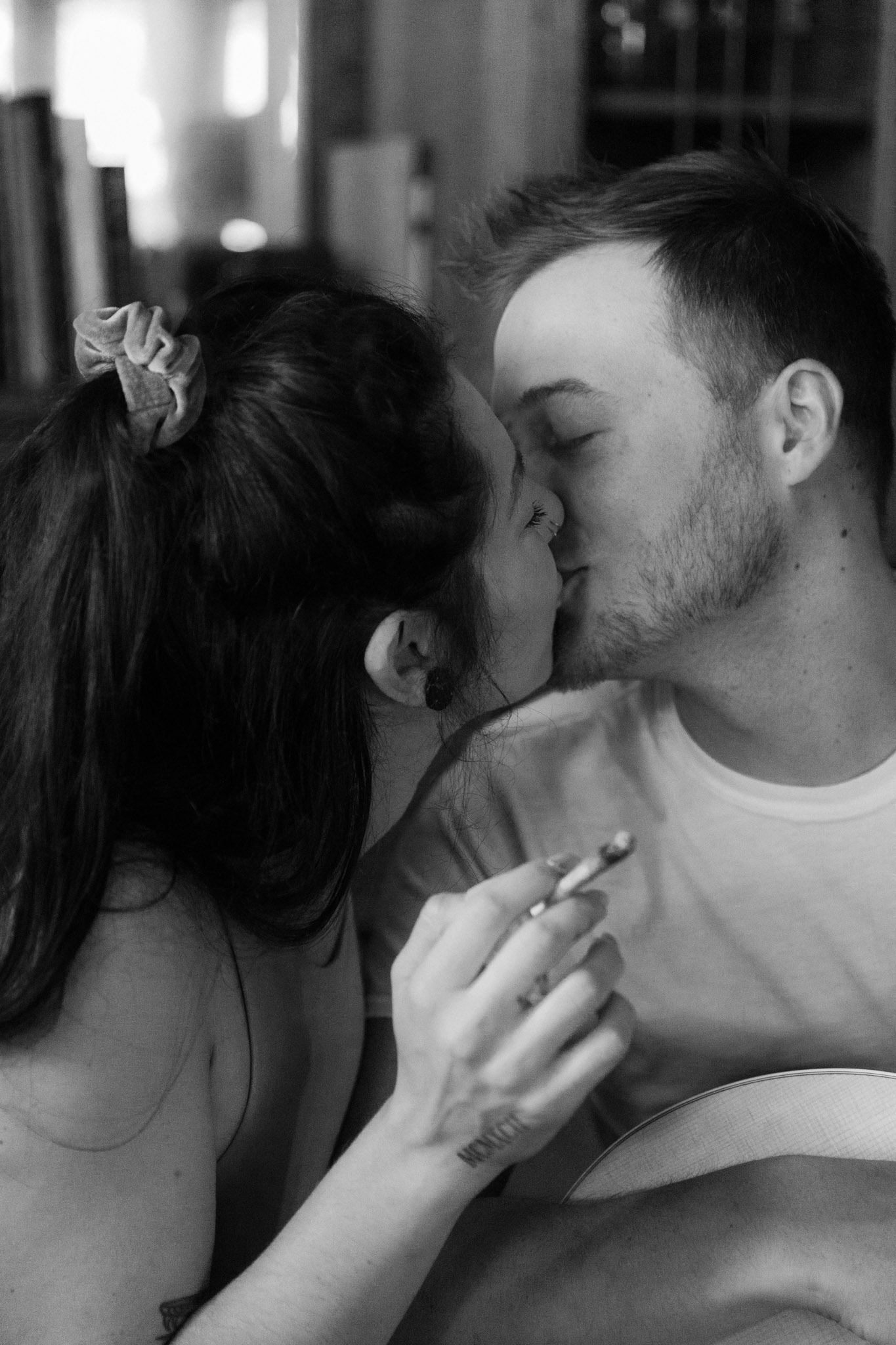 Black and white photo of a couple kissing with a joint betweenthem