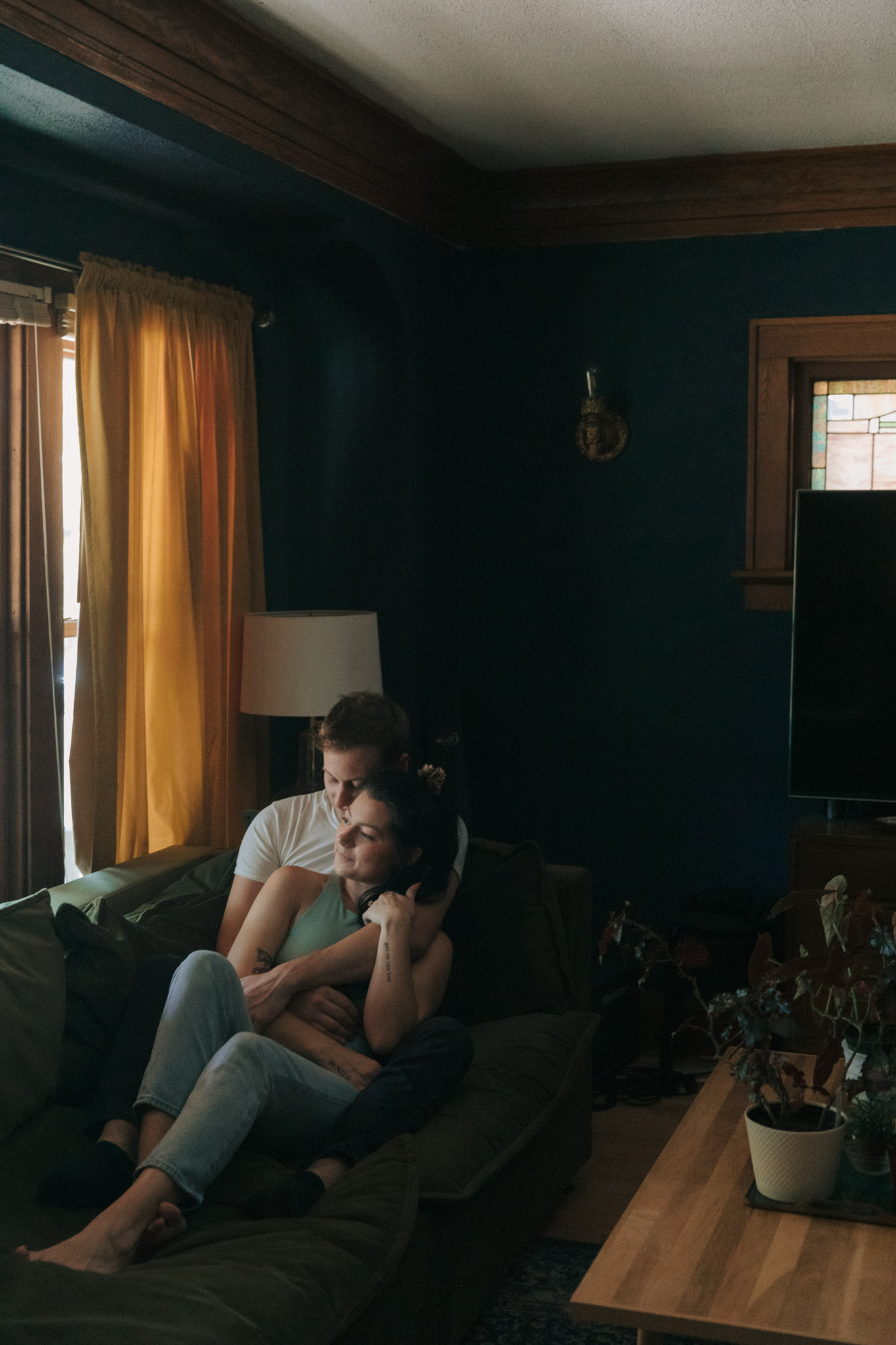 Couple sitting on a green couch with blue walls and yellow curtains behind them