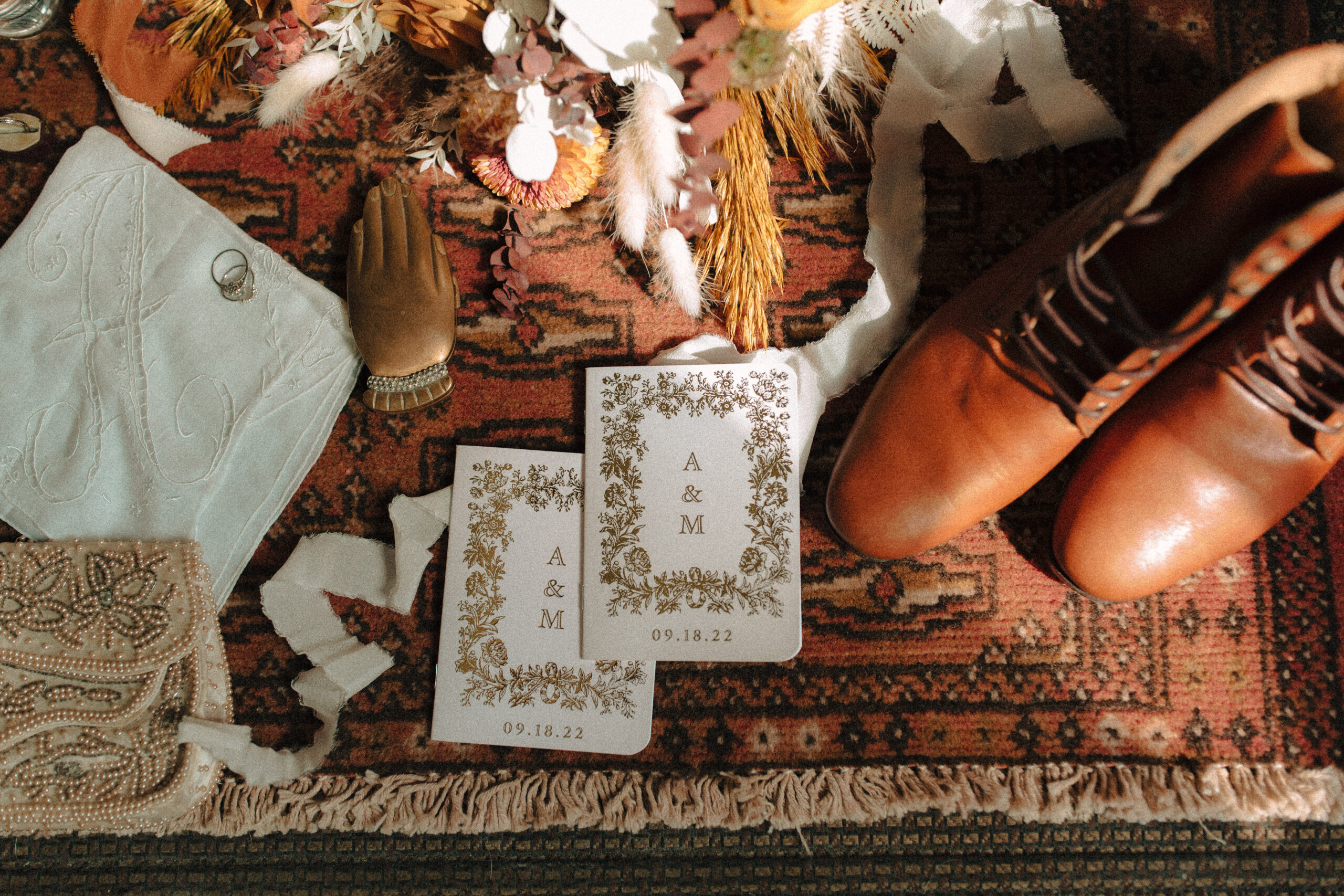 Vintage wedding flatlay details including men's vintage wedding band, monogrammed hankie, retro green sunglasses, boho bouquet, personalized vow booklets, and beaded vintage clutch
