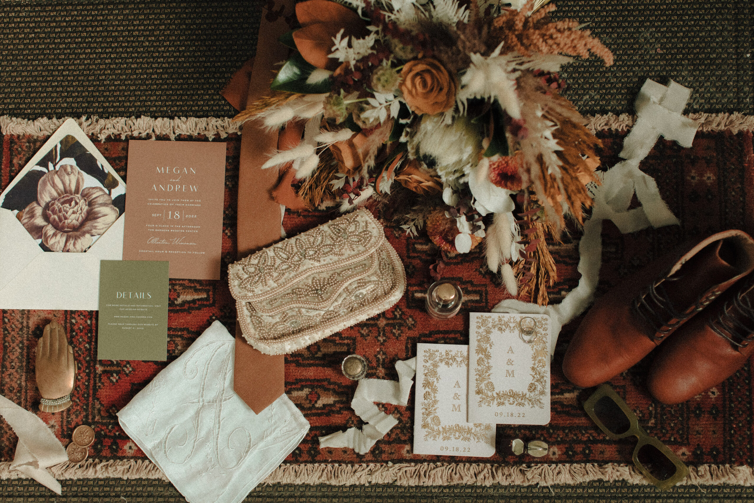 Vintage wedding flatlay details including men's vintage wedding band, monogrammed hankie, retro green sunglasses, boho bouquet, personalized vow booklets, and beaded vintage clutch