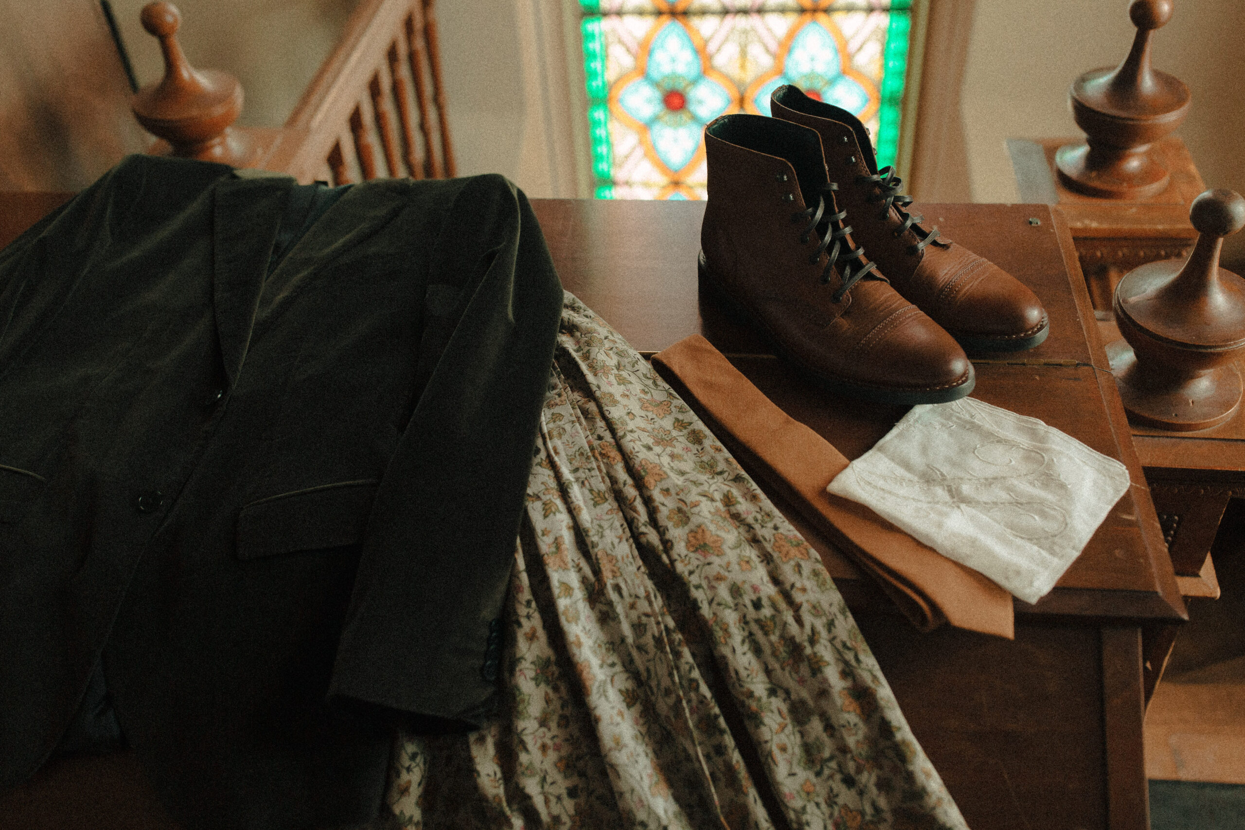 Men's vintage wedding details including green velvet suitcoat, paisley green button up shirt, caramel tie, and brown boots with monogrammed hankie