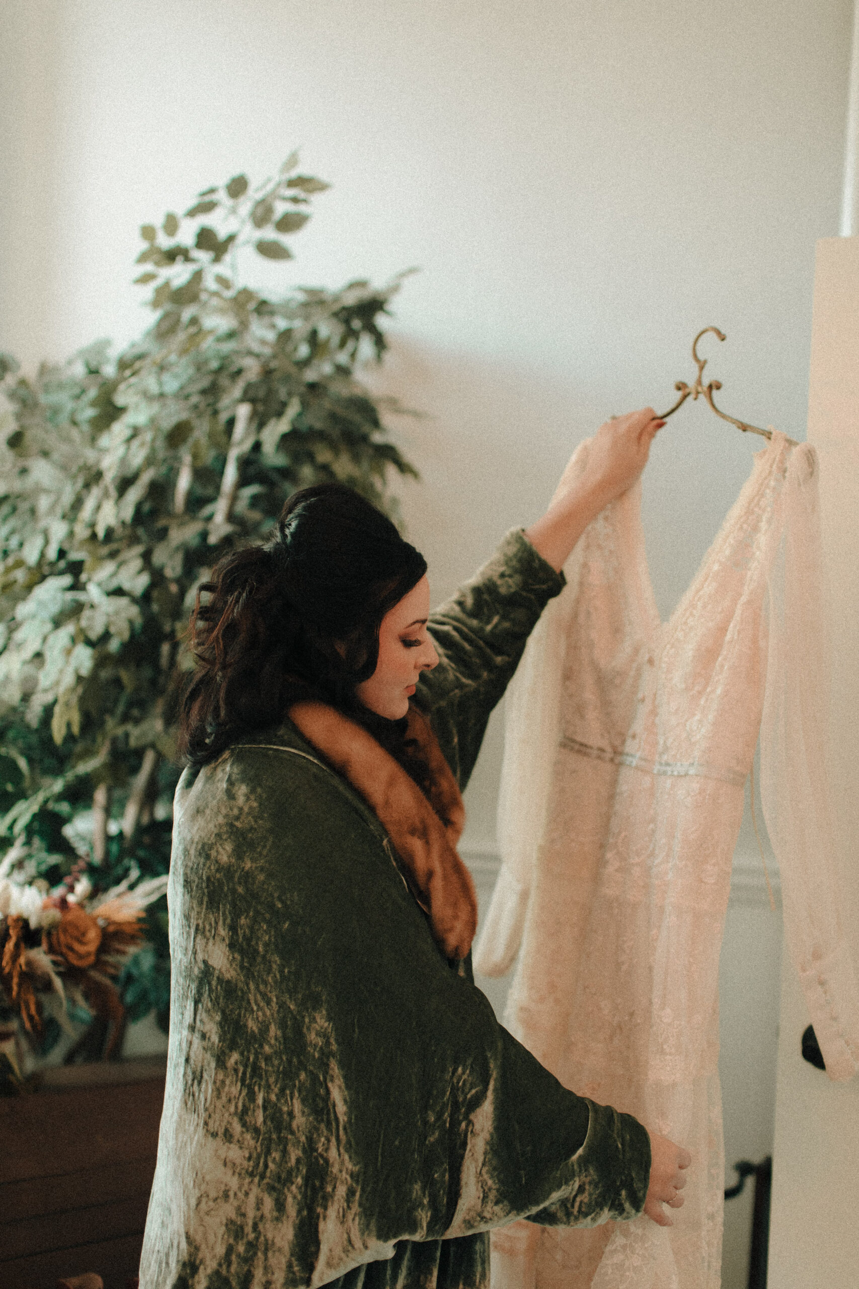 Bride with Priscilla Presley inspired retro hair and makeup wearing a green velvet robe with a fur collar and european vintage nightgown hanging up her custom designed vintage dress