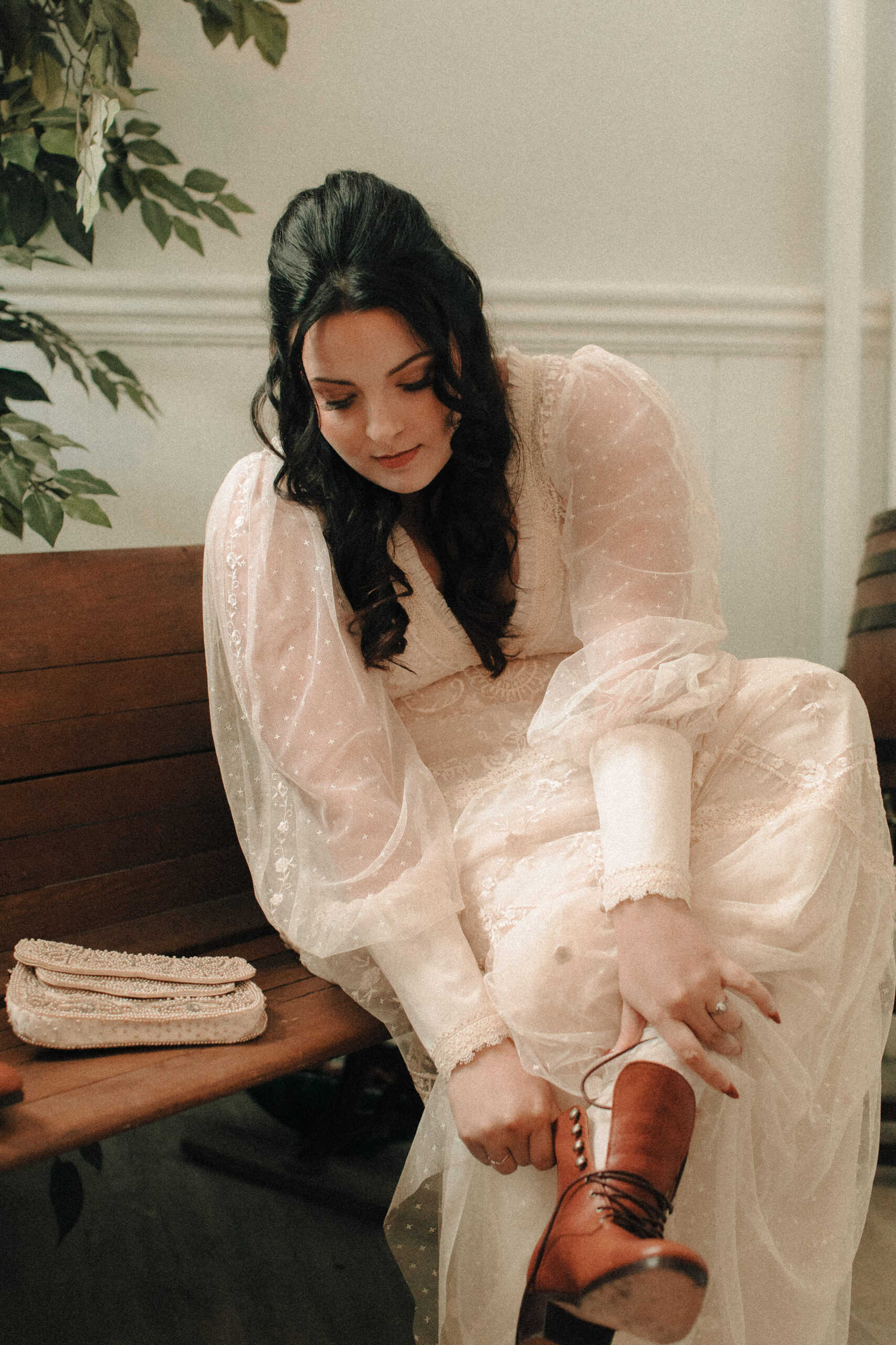 Bride wearing vintage wedding boots and creamy flowy gown with a vintage beaded clutch putting on her shoes