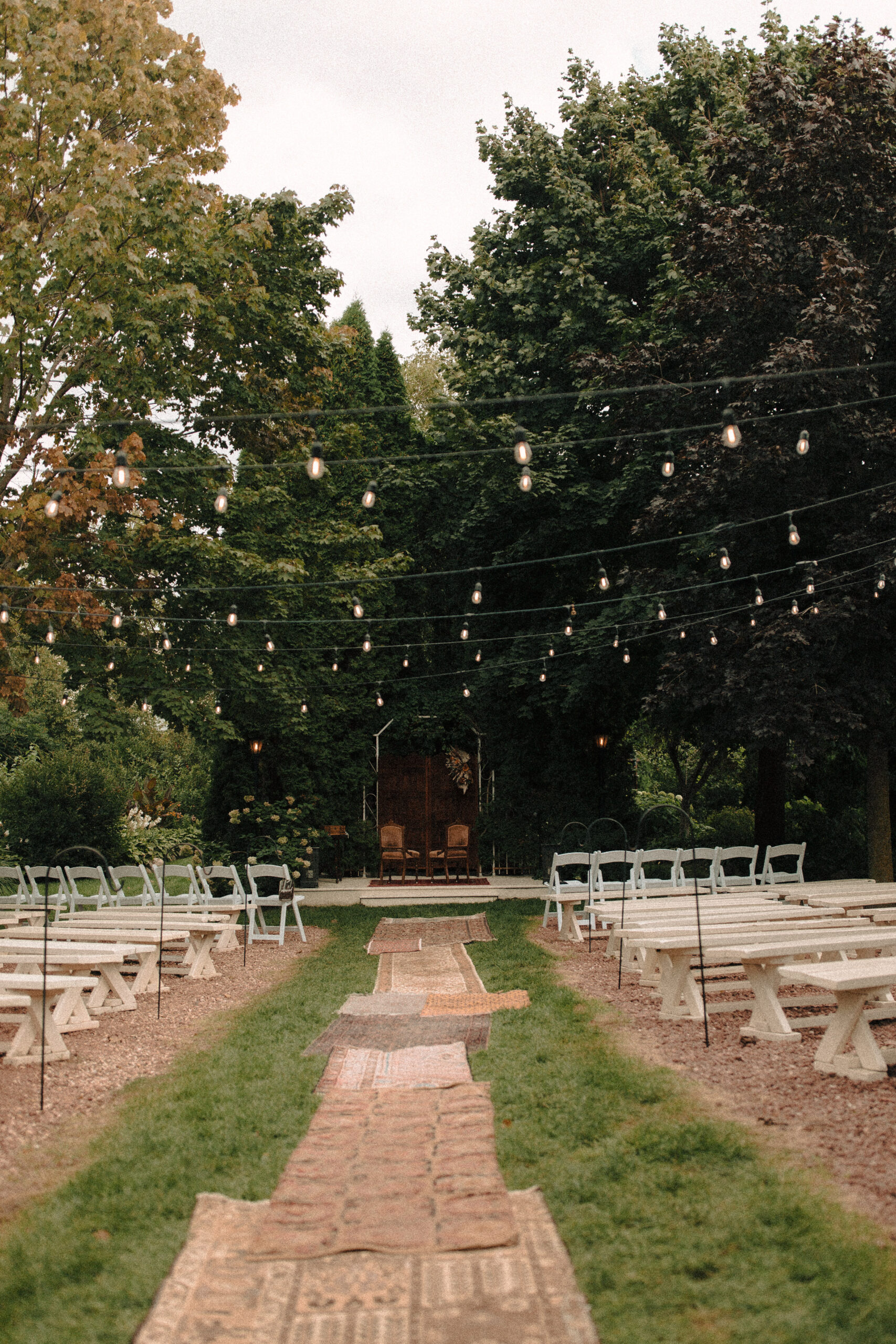 Wide view of a garden wedding ceremony with a vintage rug aisle runner and hanging fairy lights