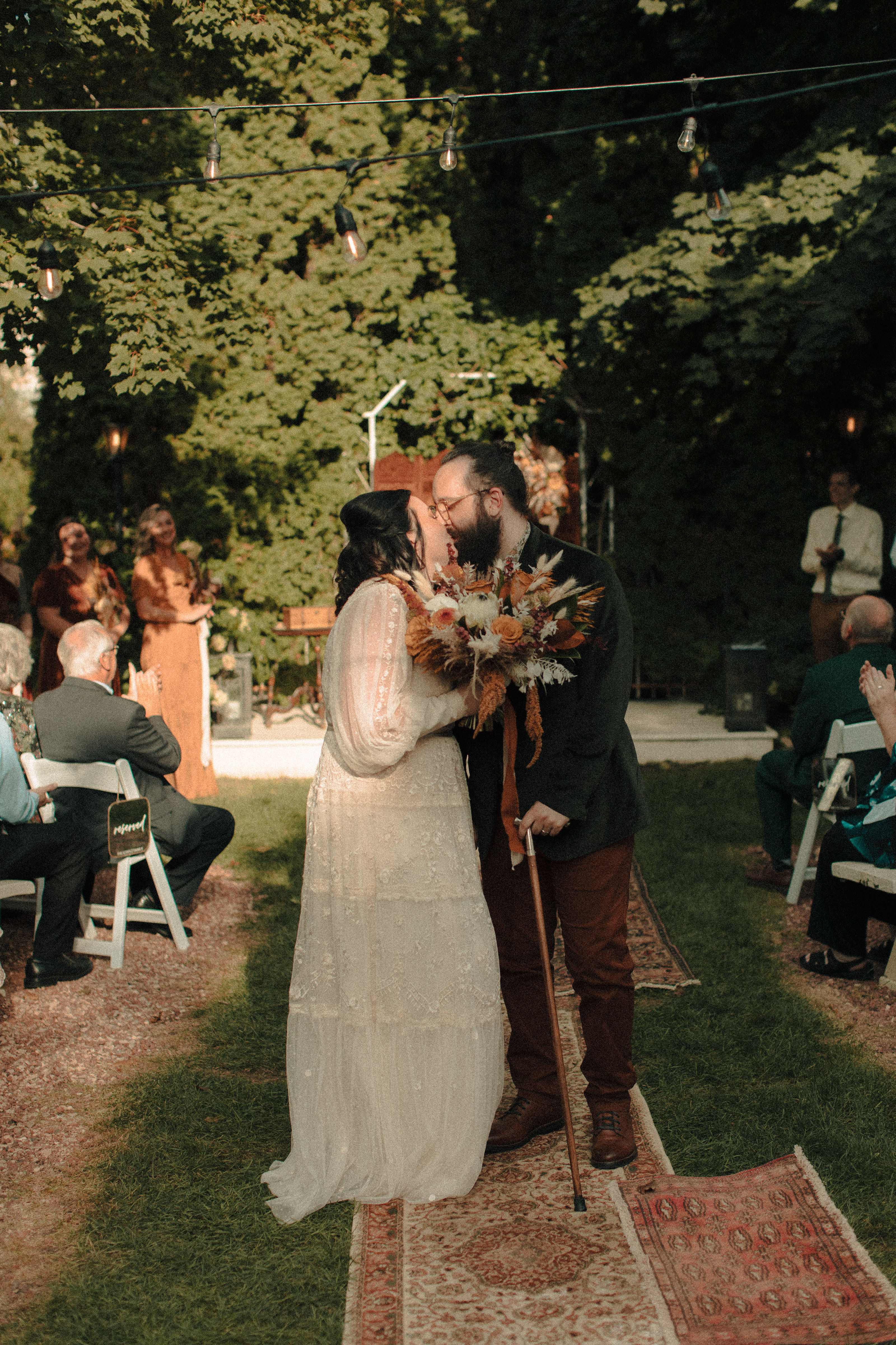 Couple kissing in the middle of the aisle after their marriage ceremony, under twinkle lights in a garden