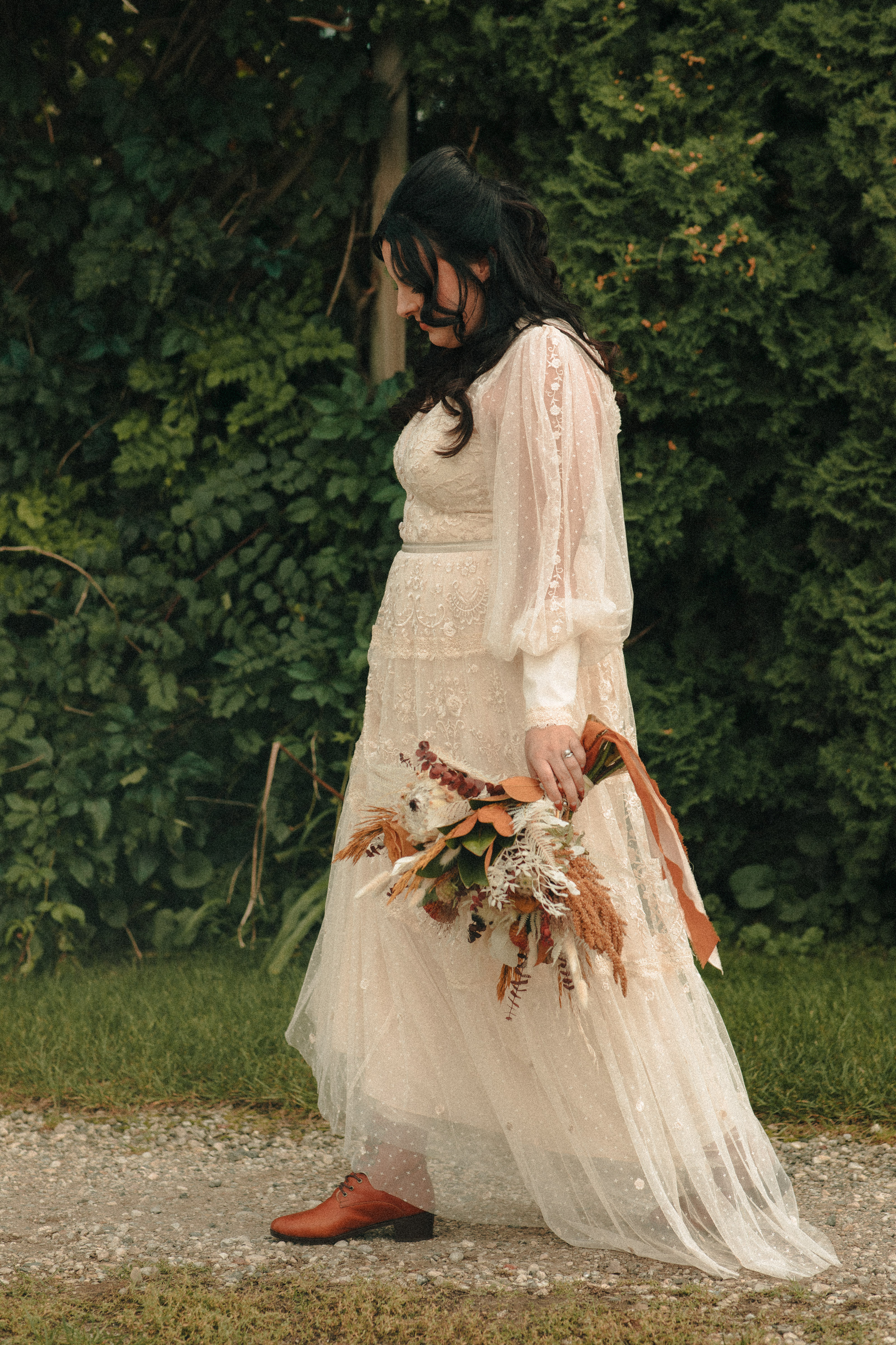 Bride in flowing vintage dress walking, wearing boots and holding her bouquet