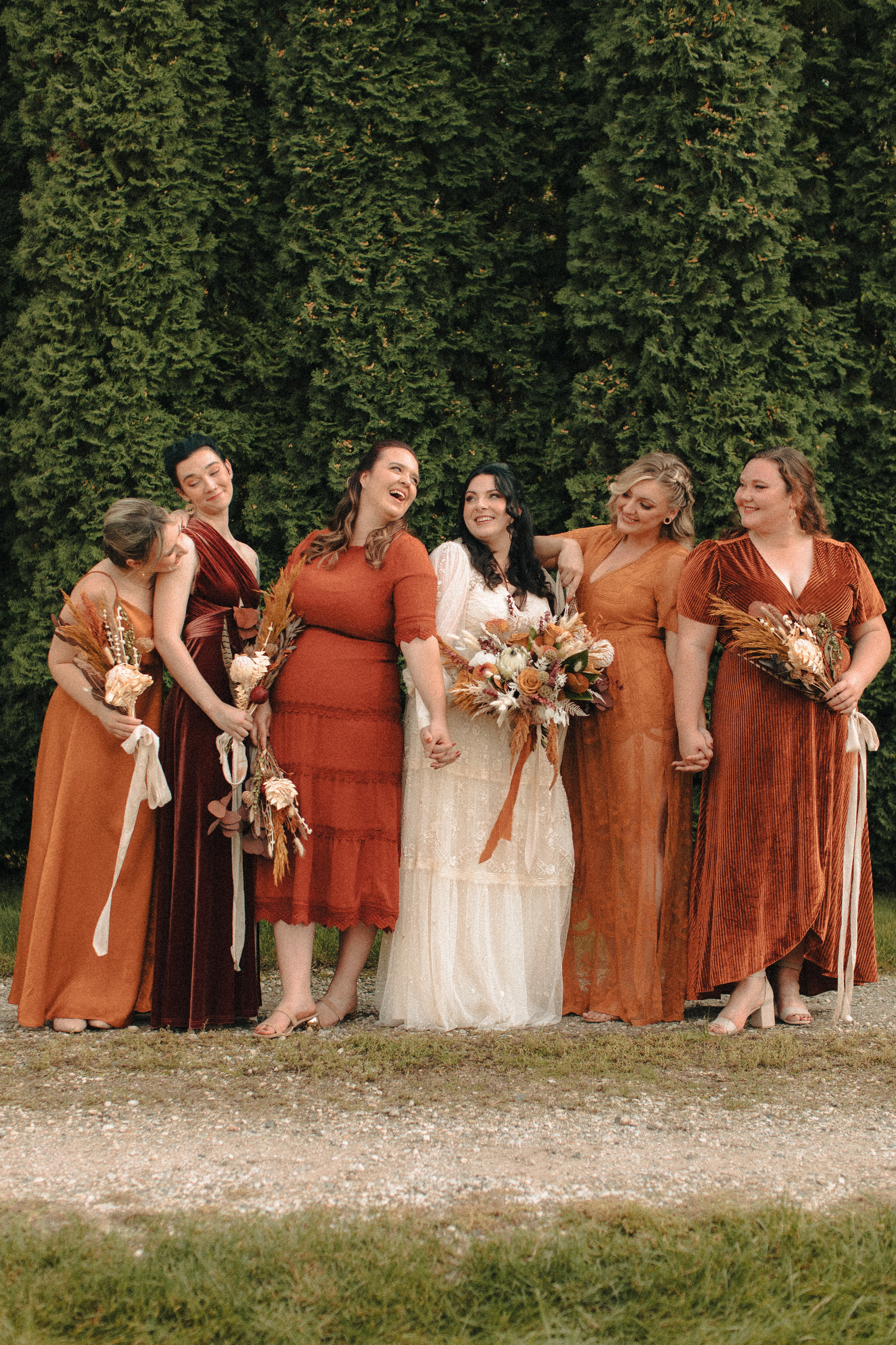 Bridesmaids in mismatched orange, rust, caramel, and gold dresses, with different textures and lengths