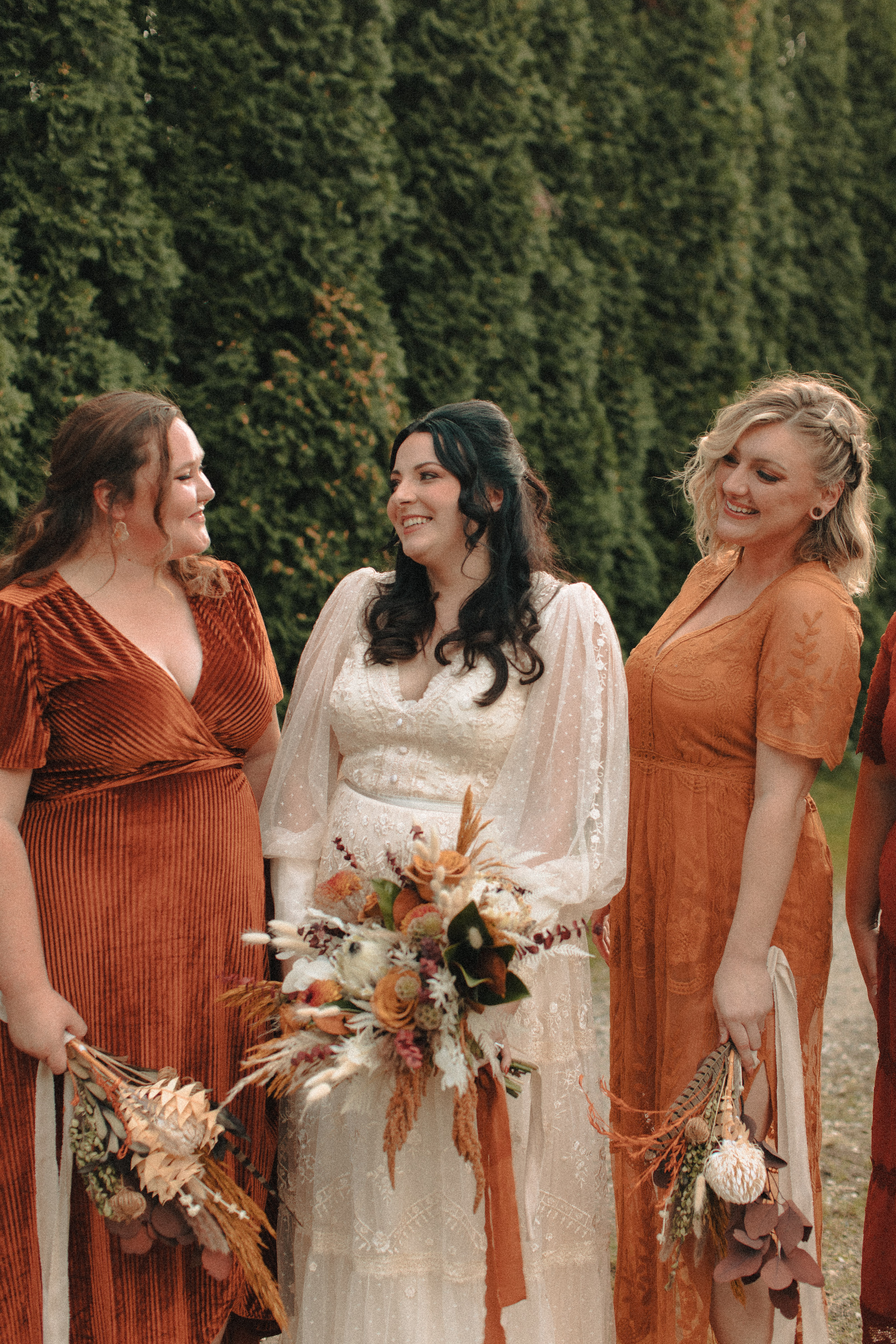 Bridesmaids in mismatched orange, rust, caramel, and gold dresses, with different textures and lengths