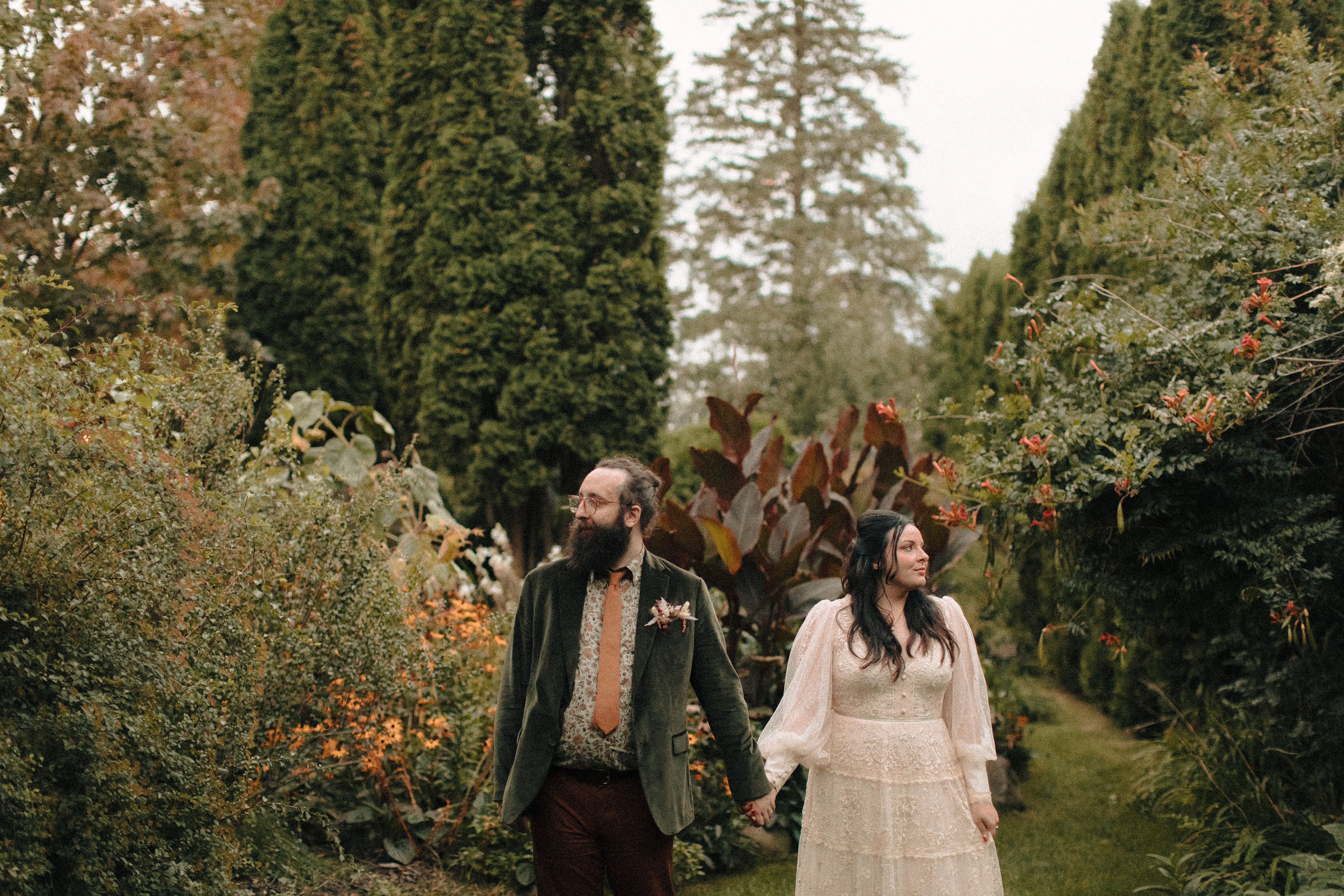 Hipster couple holding hands for wedding photos in a garden