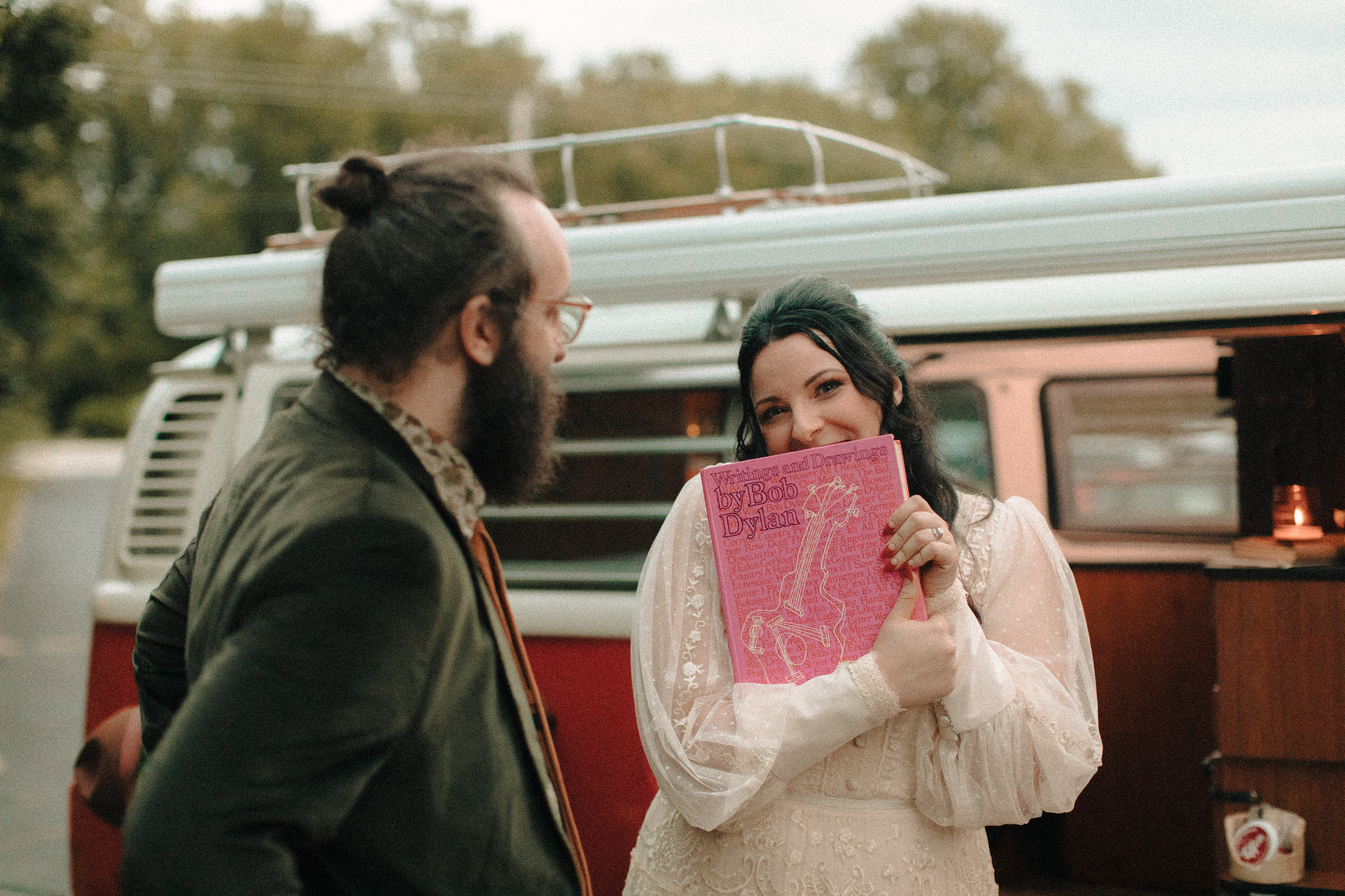 Bride in front of a vw bus holding a bob dylan book