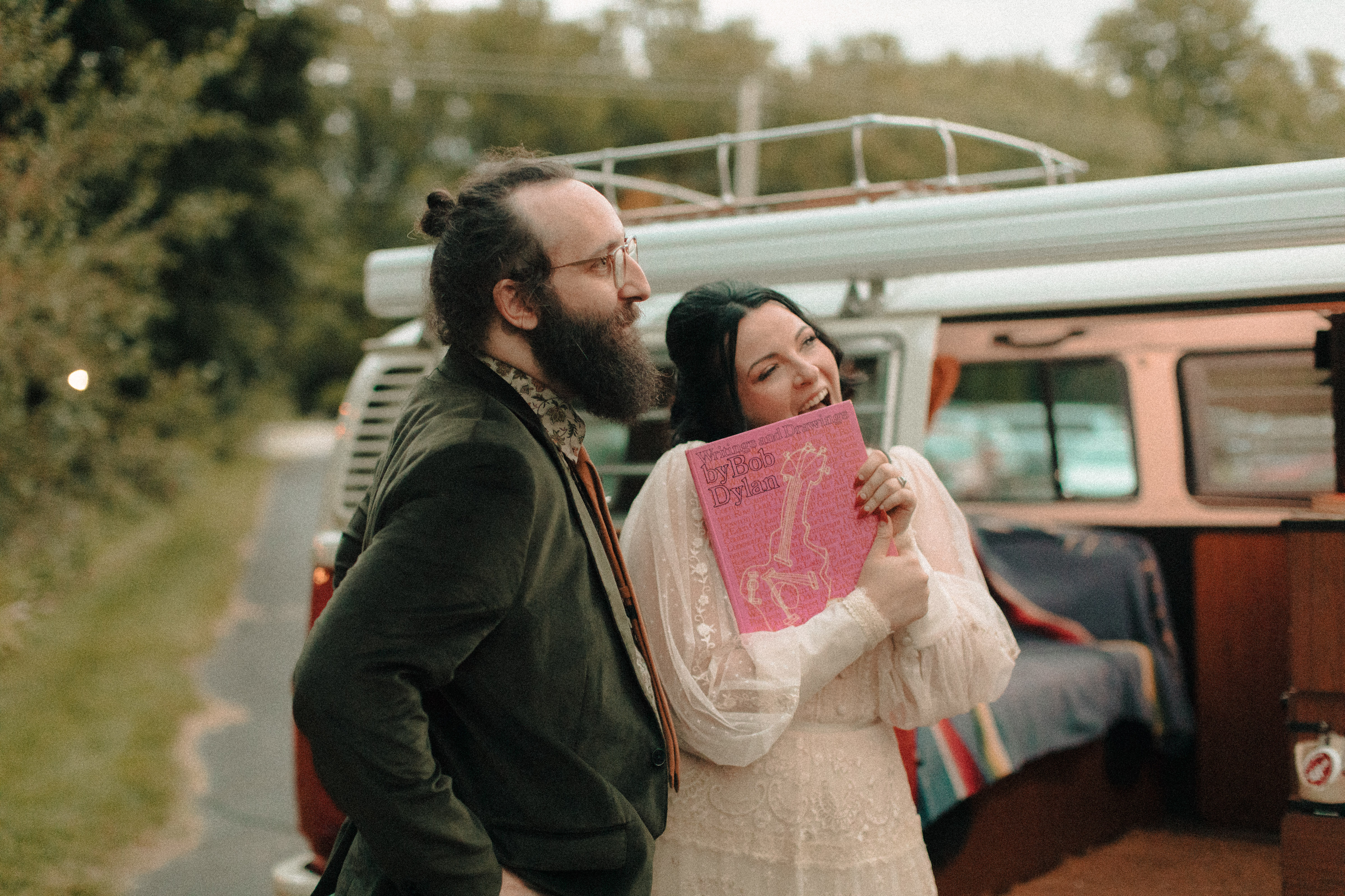 Bride in front of a vw bus holding a bob dylan book